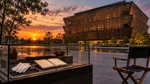 Illustrative scene of a modern African American history museum, an archival display case and an empty director’s chair at sunset.