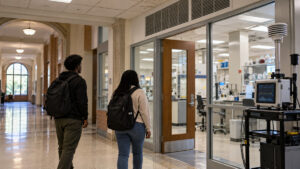 Illustrative image of two Black college students entering a university science laboratory beside an indoor air-quality monitor.